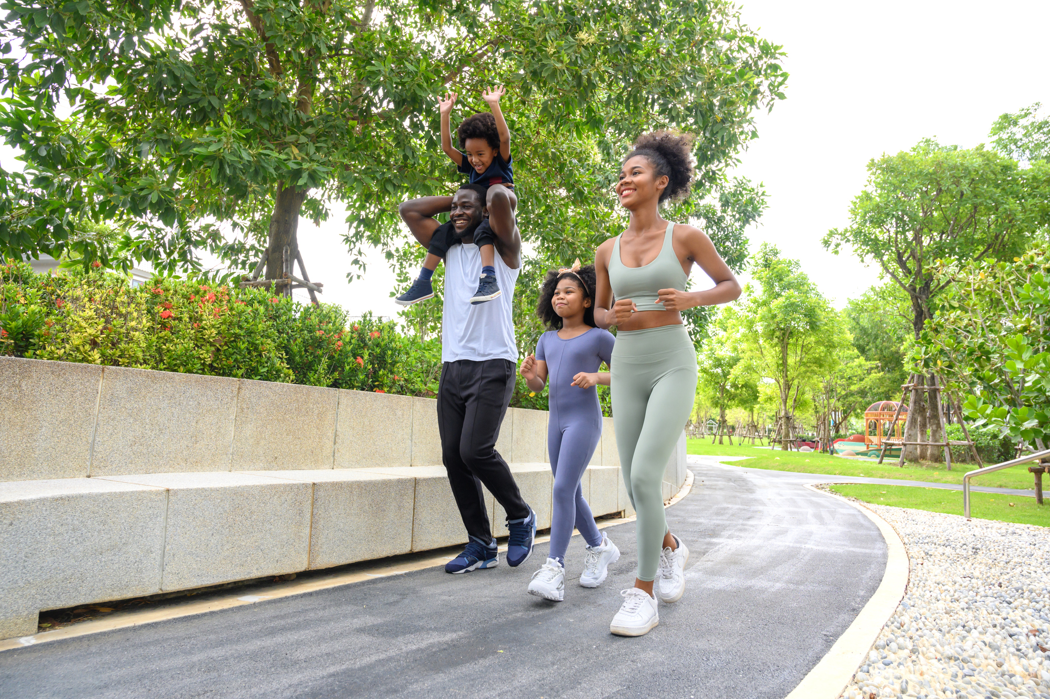 Happy African American family in sportswear running in public park. father carrying son with mother and daughter. Family exercising together concept